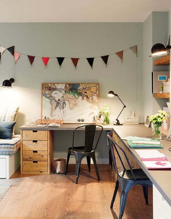 A bright home office with an L shaped desk, black metal chairs, a bunting, open shelves and decor