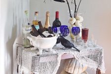 a colorful Halloween bar cart with cheesecloth, neutral pumpkins, blue glasses, a pumpkin vase with branches and a crow
