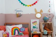 a colorful kid’s room with a color block wall, colorful bedding and toys, bright garlands and a bunny mirror