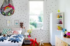 a colorful kid’s room with a polka dot wall, colorful bedding and rugs, bold toys in nets over the bed