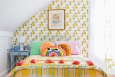 a colorful kid’s room with retro fruit print wallpaper, colorful bedding, artworks, tassels and a blue nightstand