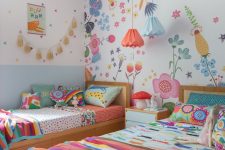 a colorful twin kid’s room with a floral statement wall, colorful bedding and pillows, pendant lamps and a tassel garland