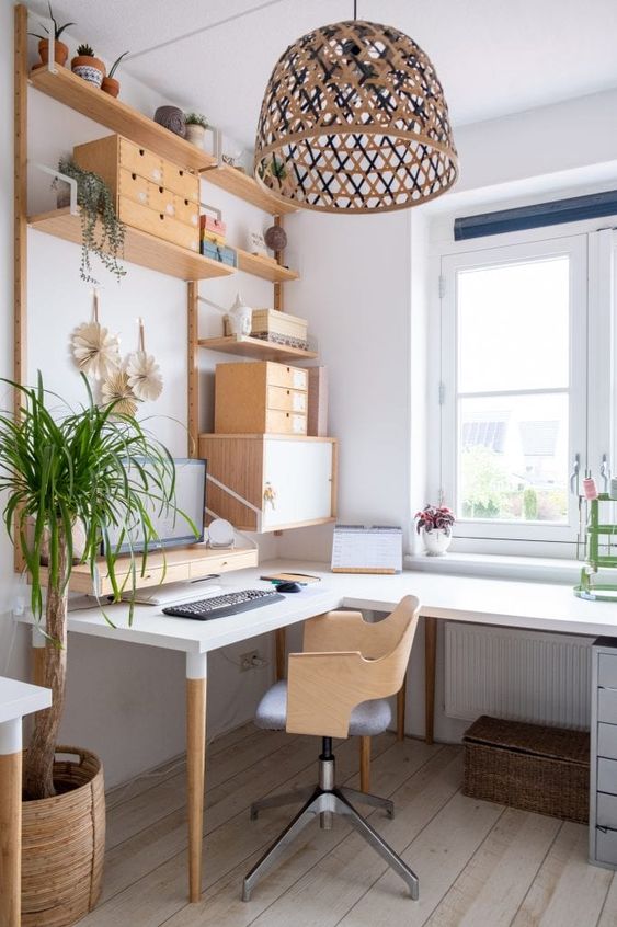 A creative Scandinavian home office with an L shaped desk, a stained chair, open shelves and drawers, a pendant lamp
