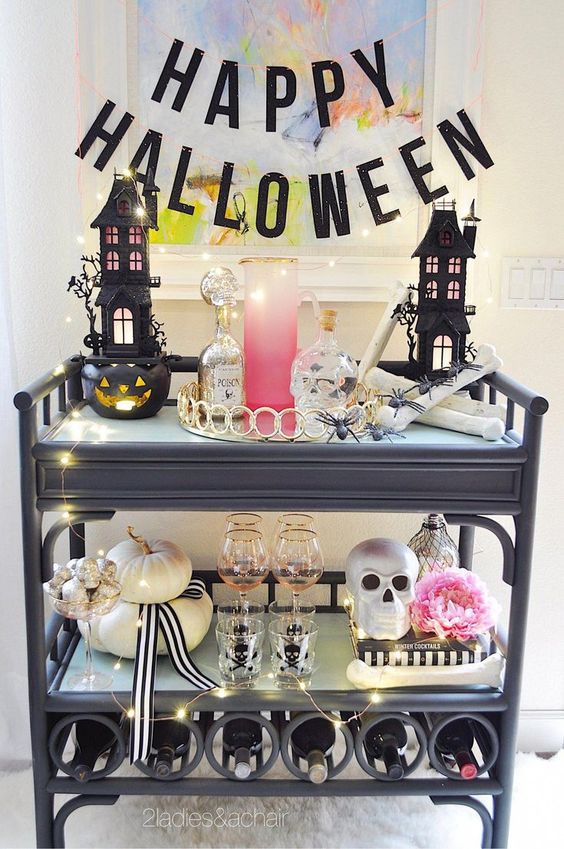 a glam Halloween bar cart with scary houses, skulls, a pink bloom, neutral pumpkins, lights and a black letter banner