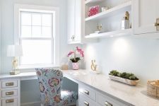 a glam farmhouse home office with white cabinetry, a large L-shaped desk, a printed chair, some decor and a cool gold chandelier