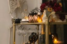 a haunted Halloween bar cart with candles, black pumpkins, a dark floral arrangement, copper mugs and spiders held by a skeleton