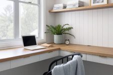 a minimal farmhouse home office with open shelves, a planked wall, a floating corner desk, a black chair and some decor