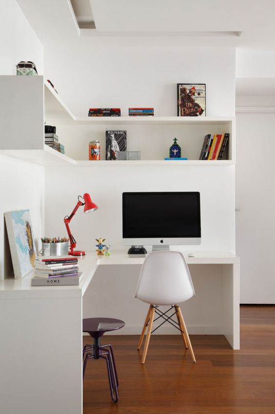 a minimalist home office with a corner desk and a corner box shelf, bright accesosries and a lamp plus a metal stool