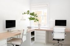 a minimalist white home office with an L-shaped desk, white chairs, storage units with drawers and potted greenery