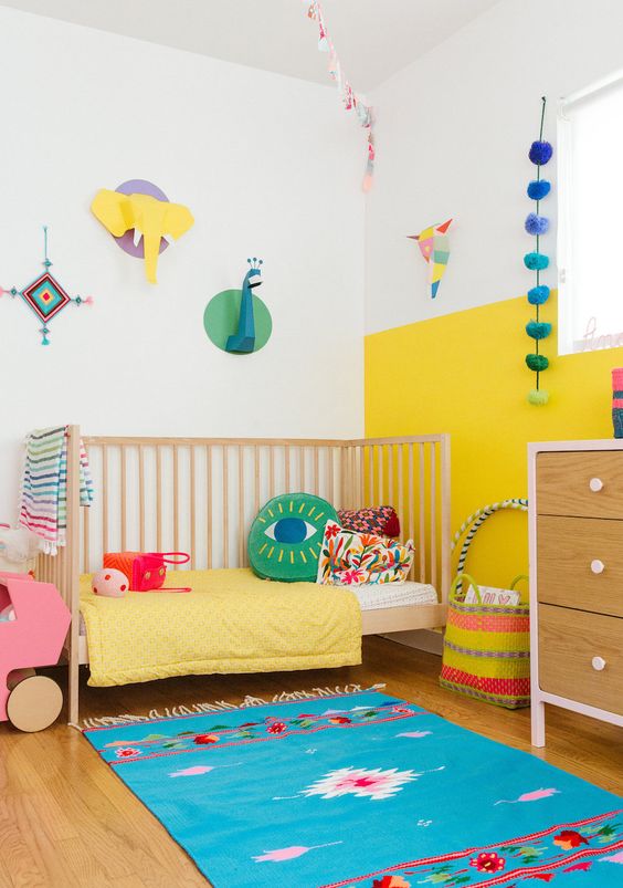 a modern colorful kid's room with a color block yellow and white wall, bright bedding and a rug, cardboard taxidermy and accessories