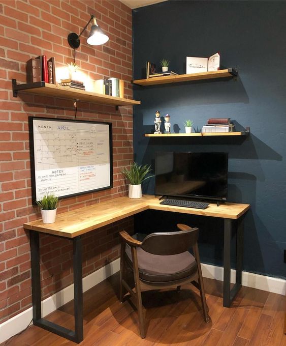 a modern industrial home office nook with a wooden corner desk and some shelves, a comfy chair and lamps