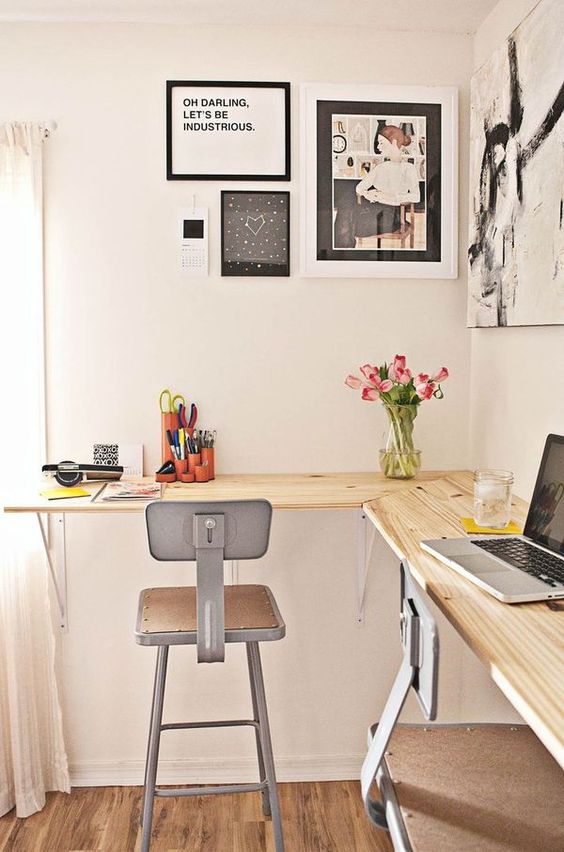 a modern industrial home office with a wooden floating desk, metal stools, a black and white gallery wall and blooms