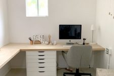 a neutral farmhouse home office with an L-shaped desk, drawers, a grey chair, a stool, jute poufs, some decor and a lamp