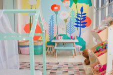 a pastel kid’s room with a bright floral wall, a mint house-shaped bed, colorful toys and a bold rug and baskets
