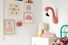 a pastel kid’s room with pastel artworks, faux taxidermy, bright bedding and a bold green bed