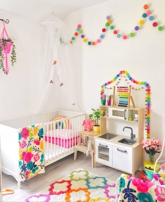 a rainbow splashed kid's room with colorful garlands, a bold rug, colorful bedding and a hot pink planter