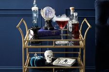 a refined Halloween bar cart with velvet pumpkins, skulls, a crystal ball, smoke and drinks
