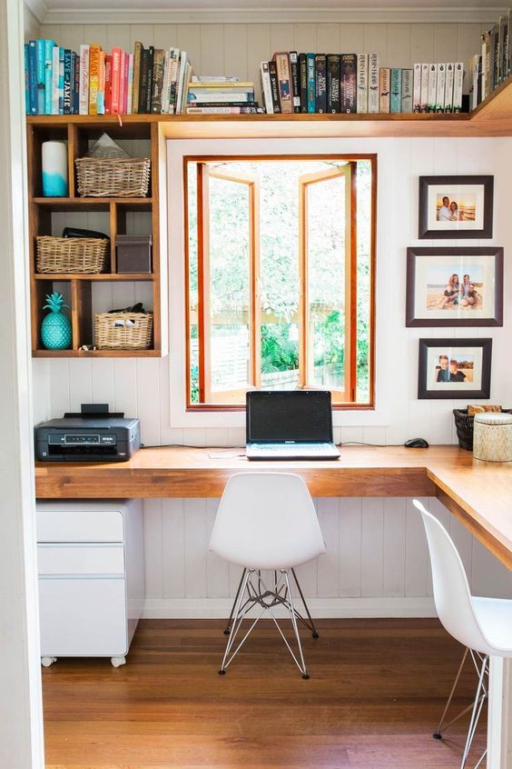 a rustic modern home office with a wooden corner desk, open shelves, white chairs and lots of books and photos