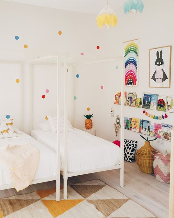 A shared kid's room done in neutrals but spruced up with brights   polka dots on the wall, colorful art, garlands and books