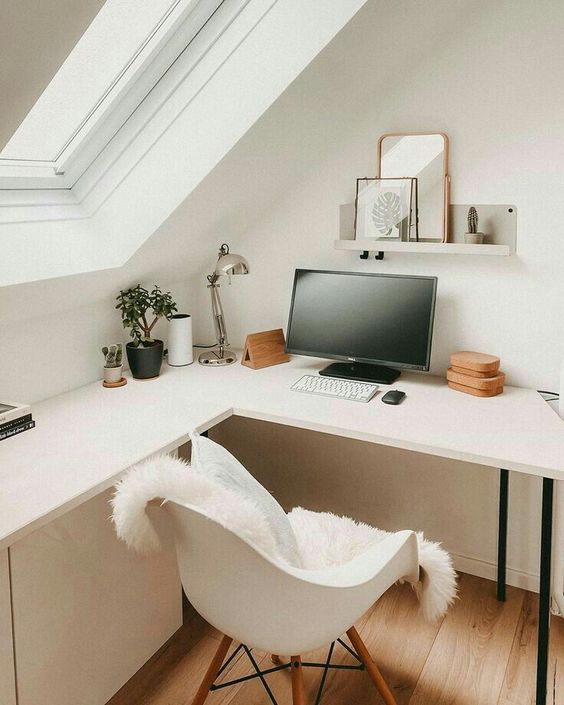 A small Scandinavian corner working space with an L shaped desk, a white chair, a shelf with decor and some plants