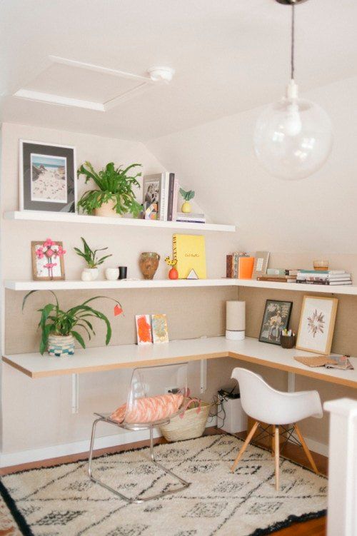 A small home office nook with open shelves and an L shaped desk, a couple of chairs, some books and decor
