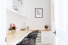 a small white home office with an L-shaped desk with storage, black chairs, a storage unt, some decor and blooms