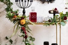 a sophisticated Halloween bar cart with greenery and bright blooms, a candelabra with candles, a black butterfly wreath and sweets and black glasses