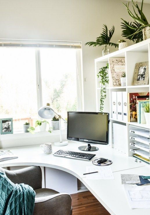a stylish contemporary home office in white, with a curved corner desk and open storage unit, a comfy chair and some greenery
