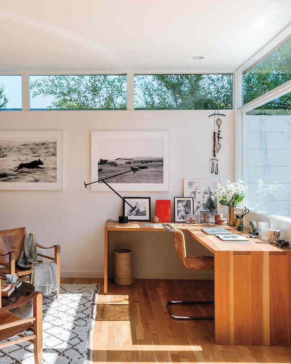 a stylish modern home office with a large corner desk with many artworks and a lovely views of outside
