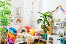 a super bold kid’s room with rainbow color garlands, matching bedding, blankets and pillows, a colorful rug and artworks
