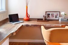 a warm-colored home office with a live edge corner desk, a yellow chair, open shelves and an orange vase