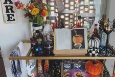 a whimsical bar cart with orange and purple decor, black and white pumpkins, bright napkins and plates and bold blooms