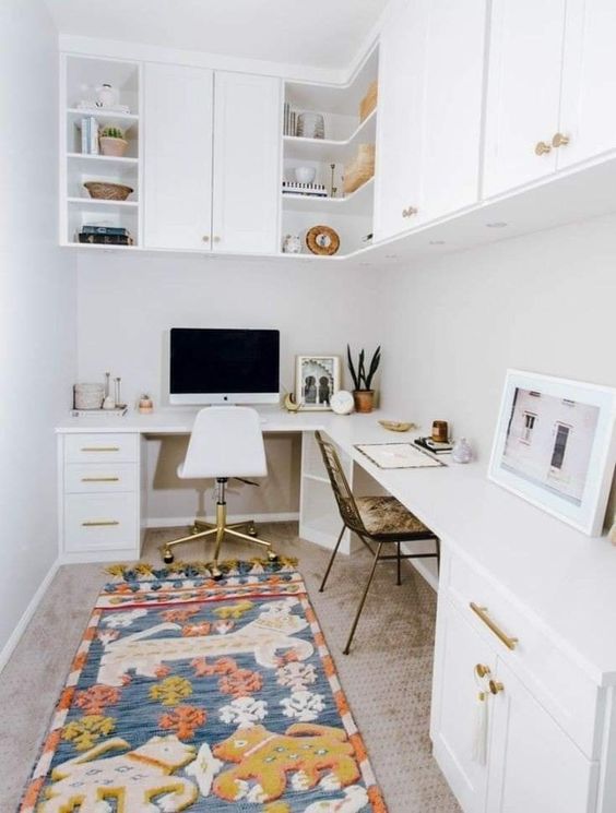 A white boho home office with an L shaped desk with storage, kitchen cabinets for storage, a bold rug and mismatching chairs