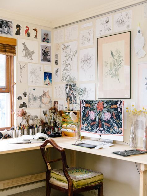 An art studio with an L shaped desk and lots of art covering the wlals, a vintage chair and a PC