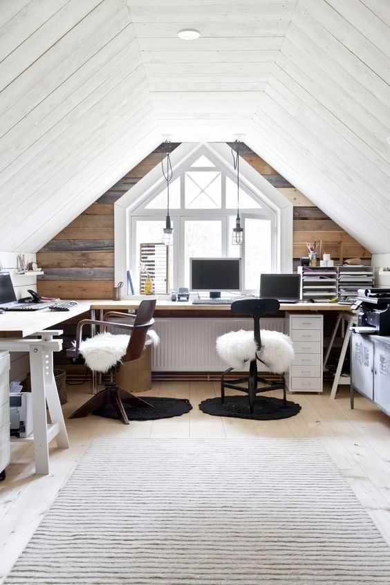 An attic farmhouse home office with a reclaimed wood accent wall, a large L shaped desk, mismatching chairs, pendant bulbs and storage units