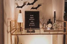 an elegant Halloween bar cart with bats on the wall, lamps and candles, white pumpkins, a sign and a crow