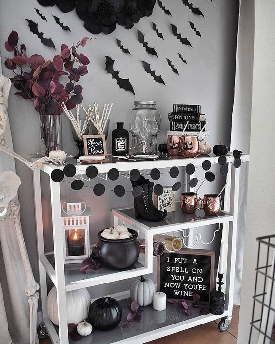 an elegant Halloween bar cart with black and white pumpkins, black dot garlands, copper mugs, bats and dark leaves