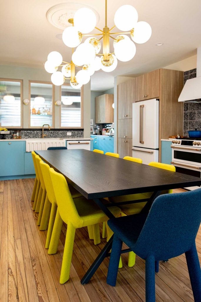 The eat in kitchen shows off blue and white cabinets, a wooden dining table and yellow and navy chairs