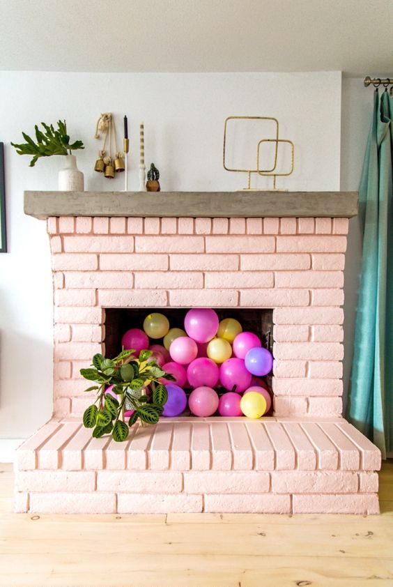 a blush brick fireplace filled with colorful balloons and with potted plants all around is a very cheerful and fun idea