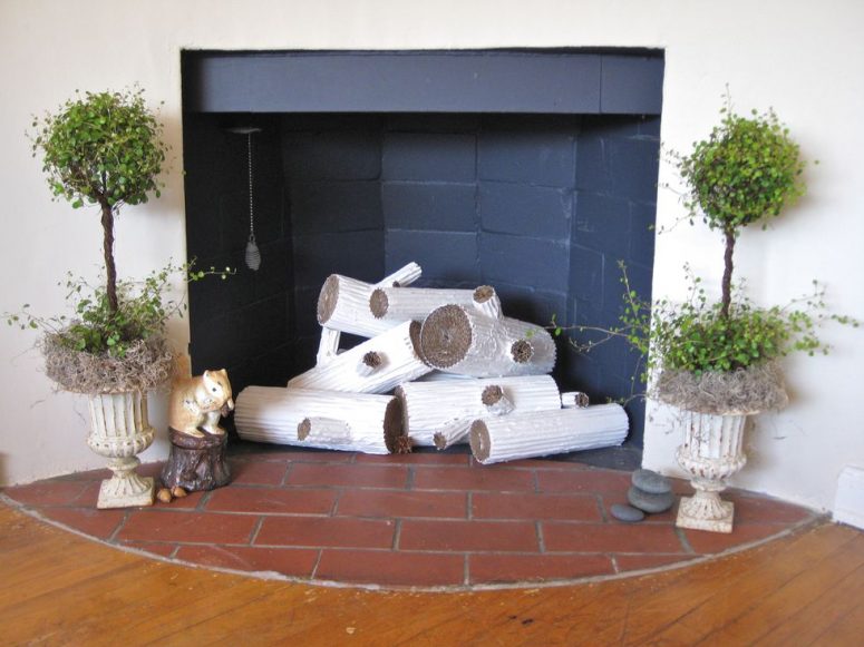 a fireplace clad with black matte tiles, with funny faux logs, topiaries on both sides and some pebbles