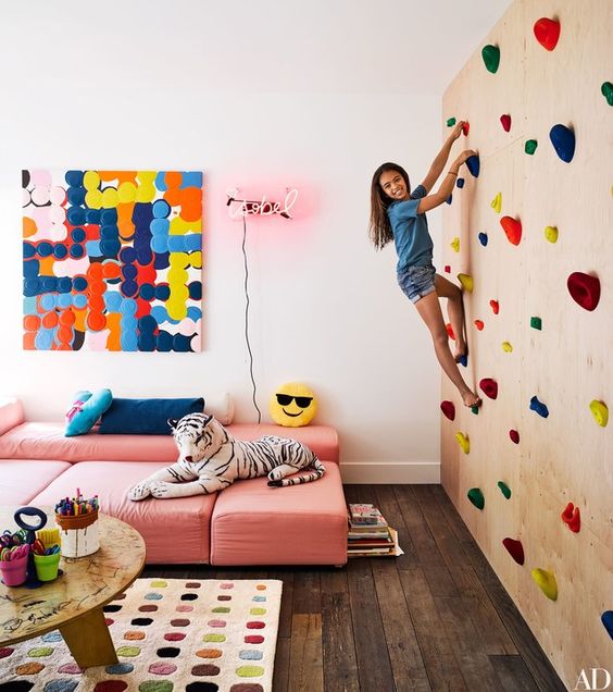 a colorful kids' playroom with a climbing wall, pink sofas, colorful artworks and a rug plus toys