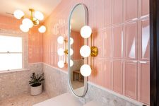 05 The bathroom is done with pink and terrazzo tiles, with retro lamps and a chandelier and a curved mirror