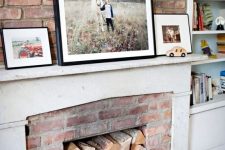 05 a rustic fireplace of red brick, with a white mantel and some firewood inside the fireplace plus photos on the mantel