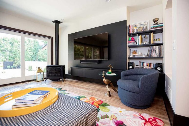 The living room with a glazed wall, which is an access to outdoors, a hearth and colorful pieces is very welcoming
