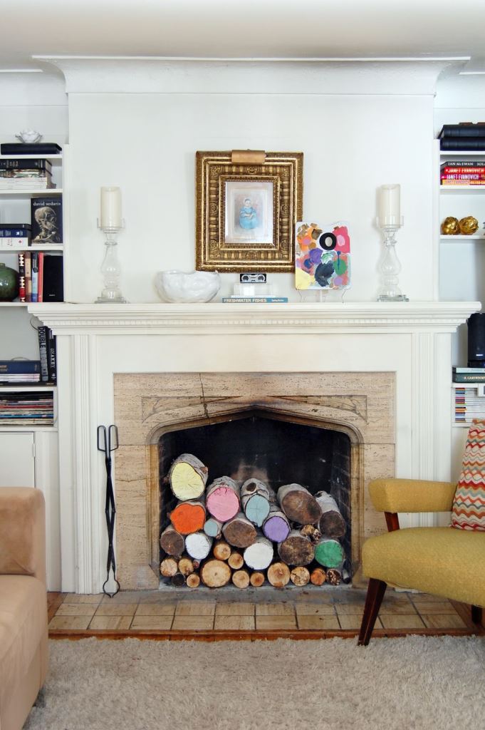 a rustic fireplace with a wooden surround, a white mantel and colorful logs inside is a very whimsical and cool idea
