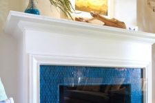 08 a fireplace surrounded with bright blue tiles, with an elegant white mantel and some coastal art on it is ideal for a seaside home