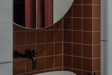 09 The bathroom is done with rust-colored tiles, a round mirror and a vessel sink