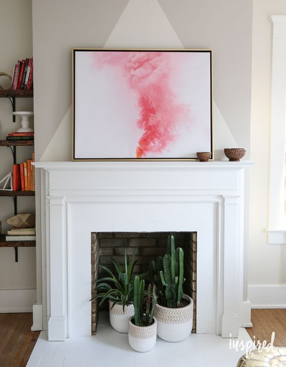 A non working brick fireplace with a white surround and mantel plus cacti and succulents in pots inside it is wow