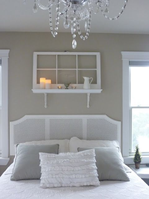 a shelf over the bed made of a shelf and an old window, some candles, a jug and more decor for a vintage white bedroom