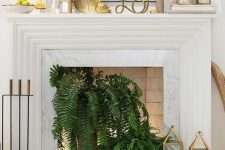 13 a non-working fireplace with potted ferns, candle lanterns, lights and gold candle lanterns and decor on the mantel